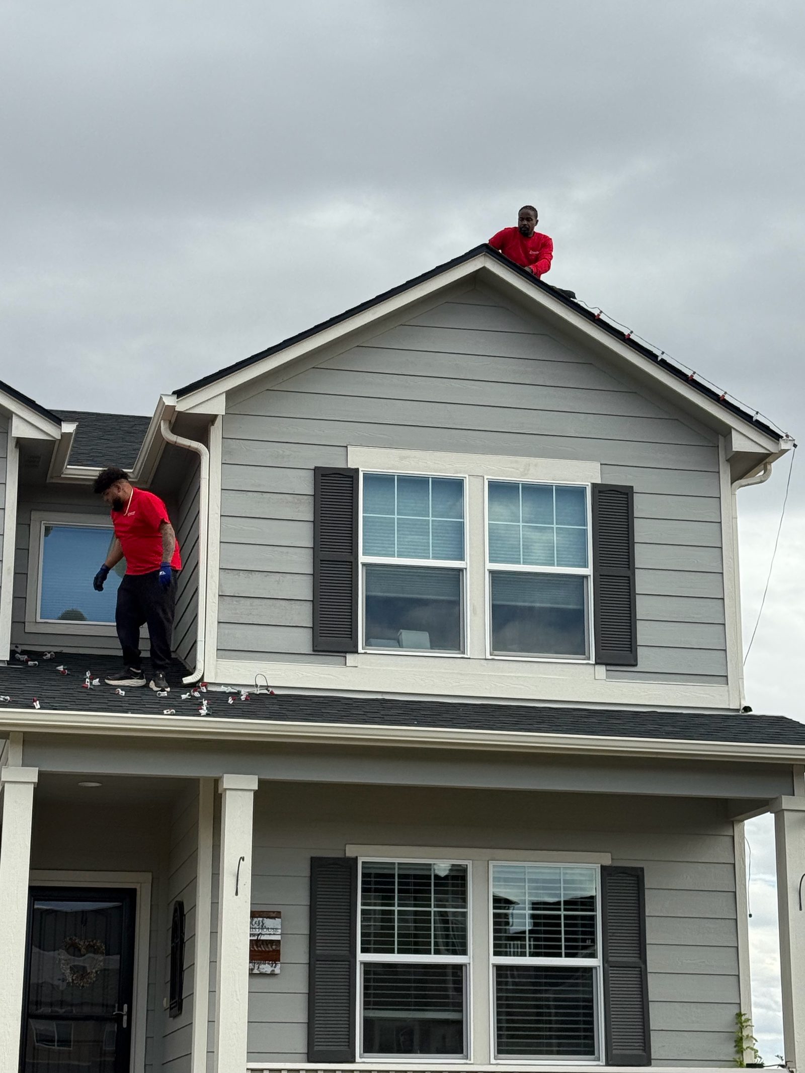 Front Range company installers on roof peak hanging holiday lights on a gray Front Range house
